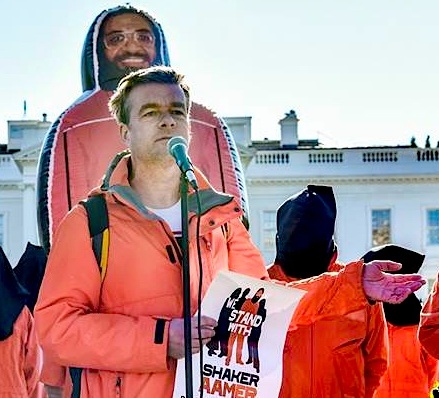 Andy Worthington speaking outside the White House on January 11, 2016, the 14th anniversary of the opening of Guantanamo. Behind him is the giant inflatable figure of Shaker Aamer that was at the heart of the We Stand With Shaker campaign (Photo: Justin Norman).