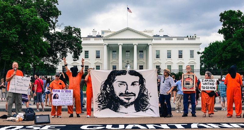 Members of the campaigning group Witness Against Torture hold up a banner featuring an image of Tariq Ba Odah outside the White House in June 2015 (Photo: Matt Daloisio via Flickr).